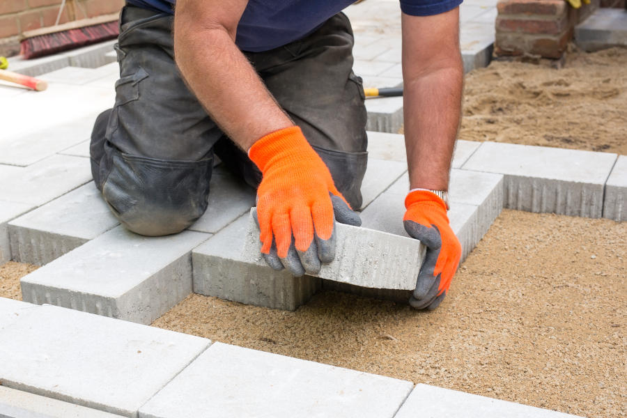 Hands of a builder laying new paving stones carefully placing one in position on a levelled and raked soil base.