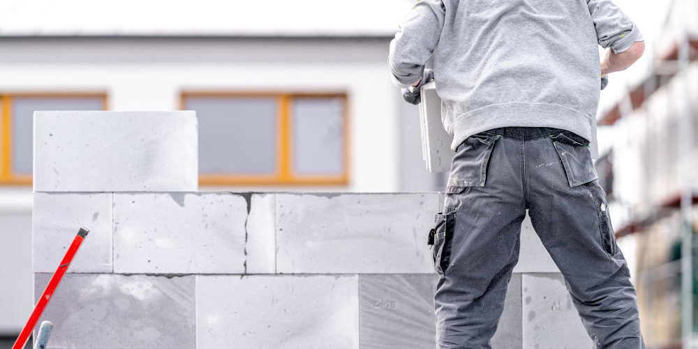 A mason builds the wall of a building from concrete bricks and blocks.